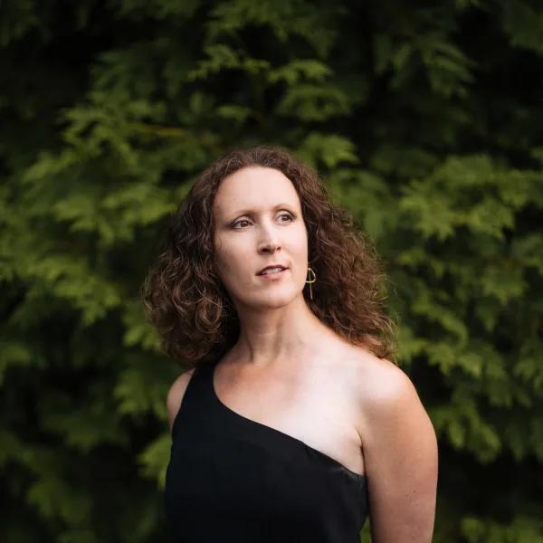 Maegan in a black dress, standing in front of green foliage